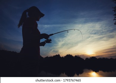 Cute caucasian woman is fishing with rod on the summer lake on the sunset
