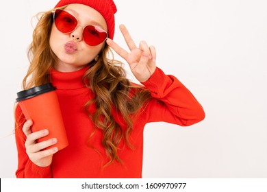 Cute Charming Caucasian Girl In A Red Winter Hat And Sunglasses Holds A Cup Of Coffee With A Mockup On A White Background