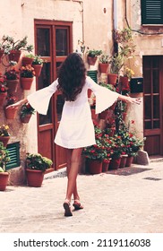 Сheerful cute charming girl walks in Spain, Mallorca. Attractive brunette with curly hair woman wears white dress. Cozy street, Valldemossa, Mallorca (Majorca) Cinematic atmosphere. - Shutterstock ID 2119116038