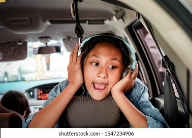 Cute And Cheerful Asian Ethnicity Teenage Girl With Headphones Enjoy Listening Music And Singing In The Car During Road Trip With Family