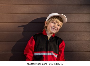 cute cheerful boy 5 years old in a red uniform of a mechanic and a white cap on the background of the garage door. smiling happy face. Sun and shadow. little helper. Be like dad. courier delivery