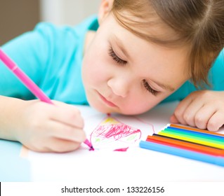 Cute cheerful child drawing using felt-tip pen while sitting at table