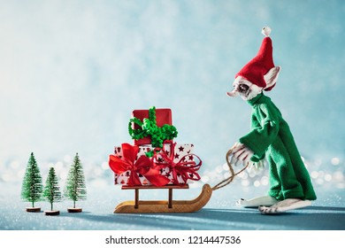 Cute Cheerful Santas Helper Elf Loading Christmas Gifts Onto Santas Sleigh. North Pole Christmas Scene. Santas Workshop. Elf At Work.