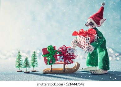 Cute Cheerful Santas Helper Elf Loading Christmas Gifts Onto Santas Sleigh. North Pole Christmas Scene. Santas Workshop. Elf At Work.