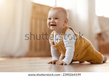 Cute cheerful smiling blonde little baby boy discovering world, crawling on wooden floor by home, copy space. Positive happy infant child playing in living room interior