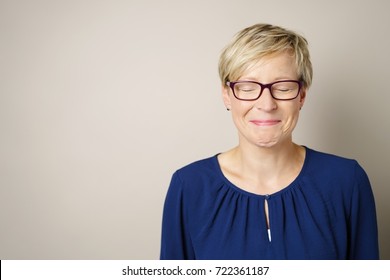 Cute Cheerful Young Woman In A Candid Portrait Closing Her Eyes With A Mischievous Grin Over A White Studio Background With Copy Space