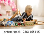 Cute child, blond toddler boy, playing with wooden trains at home