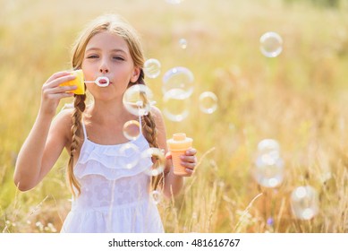 Cute Child Blowing Soap Bubbles In Meadow