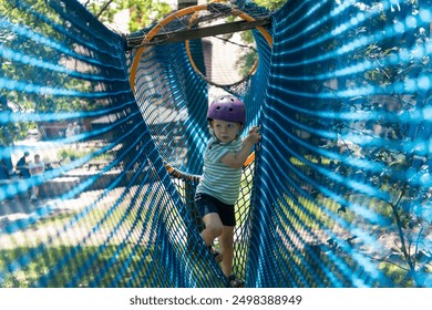 Cute child boy overcomes obstacles in rope tunnel outdoors. Modern amusement park for kids. Healthy childhood. Outdoors activities for family. Kid having fun in a rope adventure park. High quality - Powered by Shutterstock