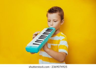 Cute child boy play the keyboard harmonica, yellow background