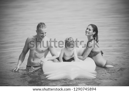 Cute child boy sits on air mattress pineapple shaped in the ocean, sea, with parents. Family vacation concept. Father and mother near mattress swim with son. Family spend time together and having fun.