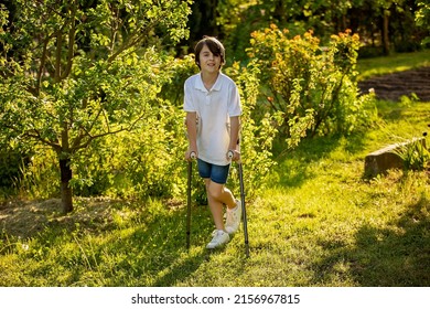 Cute child, boy, walking with crutches in a garden, having his leg injured