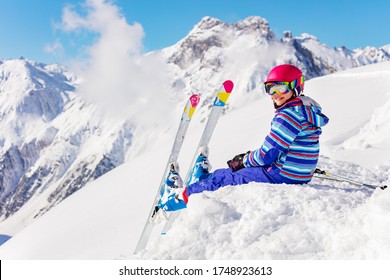 Cute Child In Bright Sport Outfit Sit On The Snow Pile In The Mountain Over High Peaks Look Back To Camera