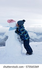 Cute Child, Building Snowman And Playing With It On Top Of Mountain, Wintertime