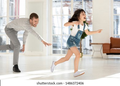 Cute Child Daughter Running From Happy Dad Catching Playing Tag And Touch Game At Home, Father Chasing Excited Kid Girl Having Fun Enjoy Leisure Activity Laughing Spend Time Together In Living Room