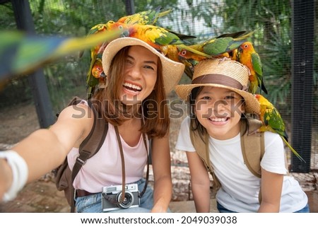 Cute child feeling happy and smiles with her mother while playing with parrot bird. Asian family portrait people. Environment human and nature concept, Smiling girl playing with pet, Sun Conure.