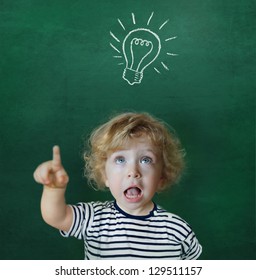 Cute child in front of a green chalkboard showing up to a light bulb - Shutterstock ID 129511157
