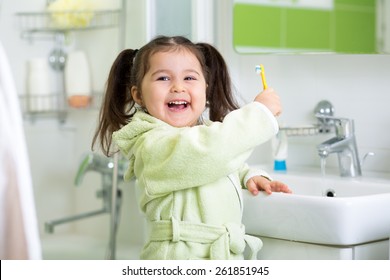 Cute Child Girl Brushing Teeth In Bathroom