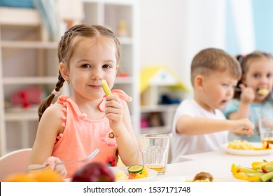 Cute Child Girl Eats Healthy Food With Kids Group In Kindergarten
