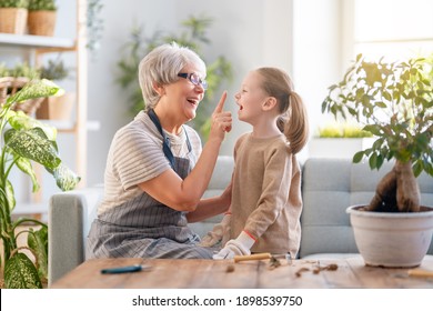 Cute Child Girl Helping Her Grandmother To Care For Plants. Granny And Her Granddaughter Engaging In Gardening At Home. Happy Family In Spring Day.