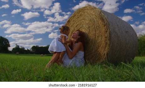 Cute Child Girl And Her Mother In White Dresses Smile In The Green Meadow. Mother And Child Enjoy With Beautiful Nature And Sun Rays At Sunset Time Together In Slow Motion Shot