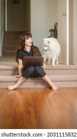 cute child girl with japanese spitz doing her online learning at home using laptop, home schooling, online education