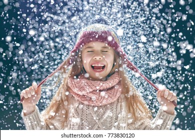 Cute child girl playing on a winter walk in nature. Portrait of happy little kid wearing knitted hat, scarf and sweater. 