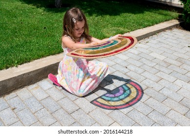 Cute Child Girl In Tie Dye Dress Playing With Rainbow Suncatcher Outside. Fun Crafting Ideas For Kids From Recyclable Items. Creative Play With Shadows. DIY Concept