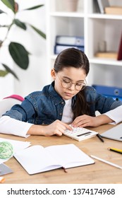 Cute Child In Glasses Using Calculator While Sitting In Office 