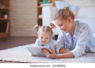 Cute Child And Her Mother With Digital Tablet Relaxing At Home