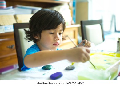 Cute Child Holding Brush To Paint On Rocks.Asian Boy Having Fun Stone Painting Activity At Home.Homeschooler's Project.Learning Art.Artistic Artwork On Stones.Young Kid Focusing On Creative Education.