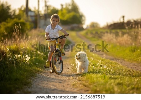 Cute child with pet dog, riding a bike in a rural field on sunset, springtime