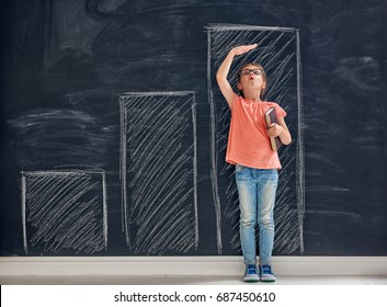 Cute child is playing. Kid measures the growth on the background of blackboard. Concept of education.