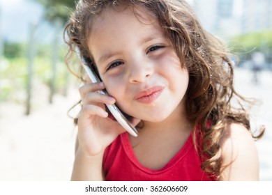 Cute Child In A Red Shirt Listening At Mobile Phone Outside