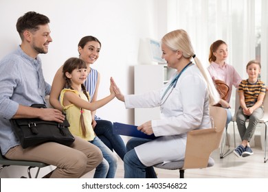 Cute Child Sitting With Her Parents And Giving High Five To Doctor In Hospital