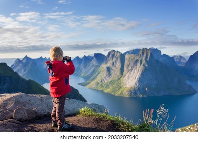 Cute child, standing on top of the mountains and looking down on Reine after climbing Reinebringen treeking path with lots of stairs, using binoculars to look at the view