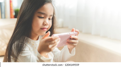 Cute child using a smartphone and smiling while sitting on sofa at home