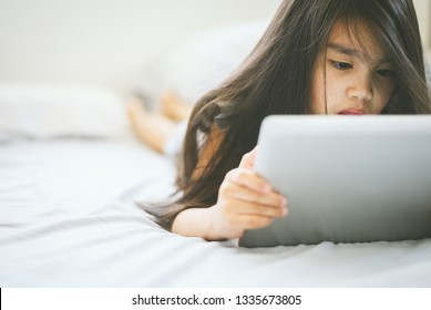 Cute child using a tablet and smiling while sitting on sofa at home