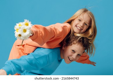 cute children, brother and sister stand sideways to the camera and the fool, the boy rolls the girl with a bouquet of daisies in his hand on his back, and she joyfully holds out her hand to the camera - Shutterstock ID 2165844743