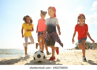 Cute children playing soccer at beach on sunny day. Summer camp