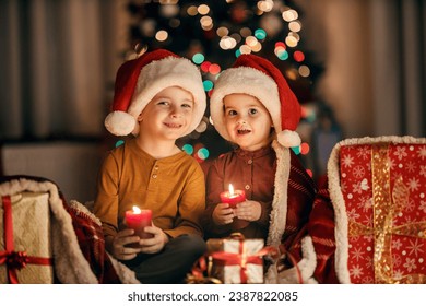 Cute children sitting at cozy and warm home with candles in hands on christmas and new year's eve and smiling at the camera. Brother and sister.