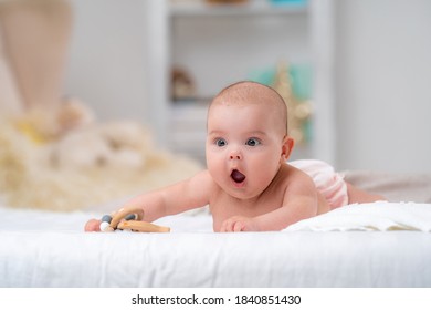 Cute chubby surprised baby of 4 months lies on his stomach with a toy made of wood and looks away. The little child was very surprised. he's learning to crawl. Copy space.