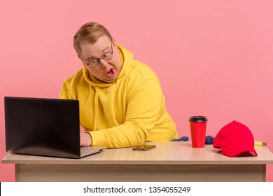 Cute comic man in bright colors casual wear geek working on computer with funny stupid facial expression