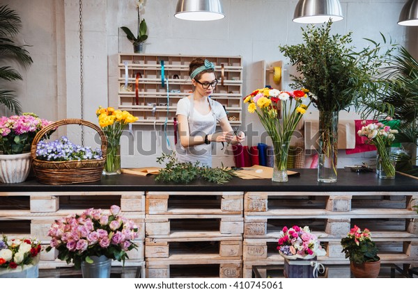 可爱集中的年轻女花店在眼镜工作在花店库存照片 立即编辑