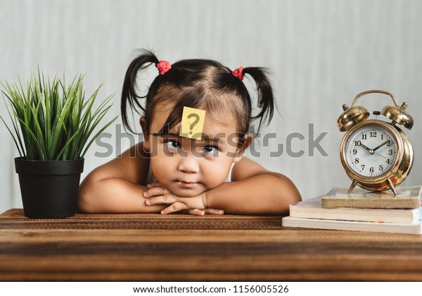 cute and confused lookian asian toddler with\
question mark on her forehead. concept of child learning education,\
growth and development.