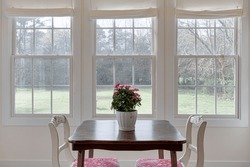 Cute Cottage Dining Room Interior With Small Wood Table, Colorful Cushioned Chairs And Large Windows Allowing Abundant Sunlight