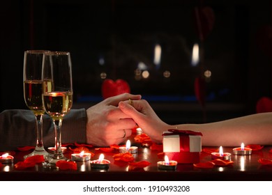 Cute couple celebrating Valentine’s Day, holding hands lovingly during romantic dinner. Red roses, gift, candles and glasses of champagne. Concept about lifestyle, people and celebrations. - Shutterstock ID 1910493208