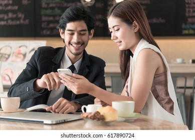 Cute couple enjoying watching on mobile phone together in cafe with coffee on the table.