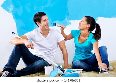 Cute Couple Painting New Home Together Portrait While Sitting On Wooden Floor