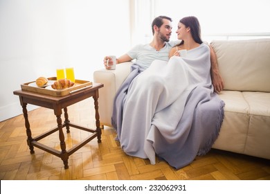 Cute Couple Relaxing On Couch Under Blanket At Home In The Living Room